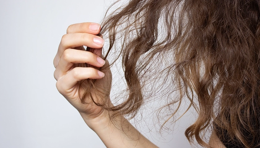 Mano sujetando un mechón de pelo encrespado y sin definición debido a la humedad..webp