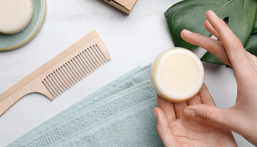 Manos sujetando una pastilla de champú sólido, ideal para viajar sin líquidos en avión como alternativa cosmética sostenible.webp