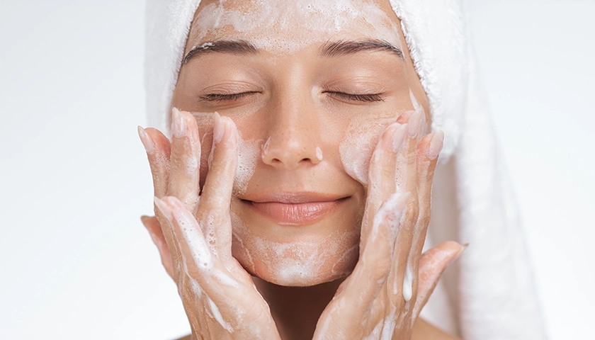 Mujer aplicándose un limpiador facial en el rostro durante la rutina de doble limpieza..webp