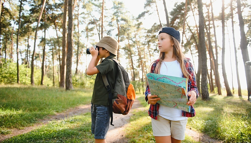 Niños caminando por el bosque con mochila y mapa durante un campamento de verano..webp